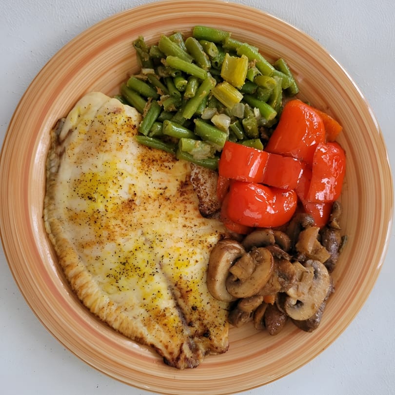 Baked fish fillet with green beans, red bell peppers, and sautéed mushrooms on a striped plate.