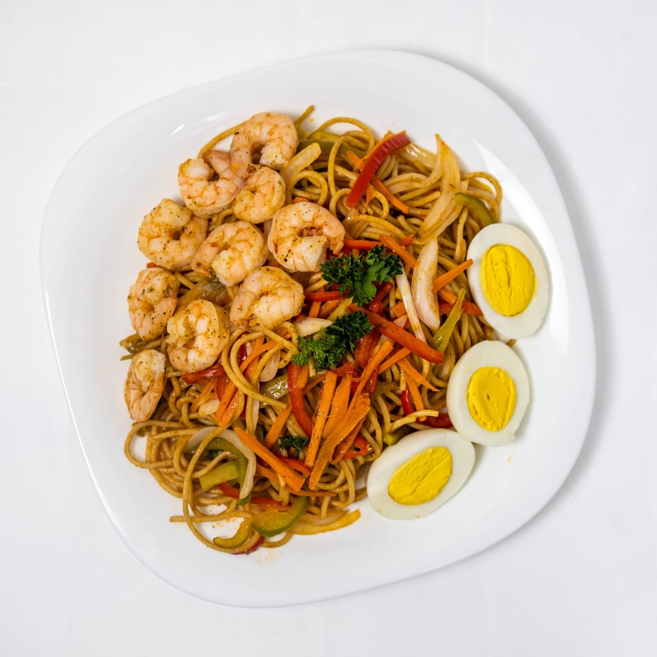 Shrimp chow mein with colorful vegetables, garnished with parsley and three hard-boiled egg halves.