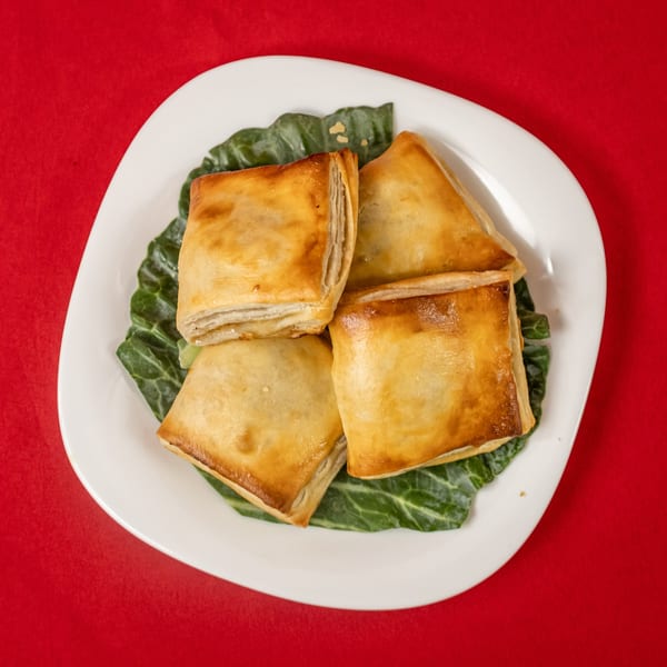 Four golden-brown square pastries on a bed of green leaves, served on a white plate.