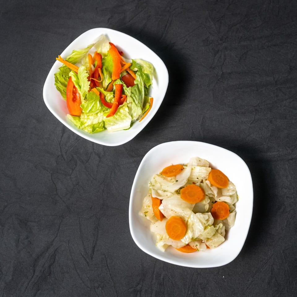 Two white bowls of side dishes: a green salad with red peppers and a cabbage and carrot mix.