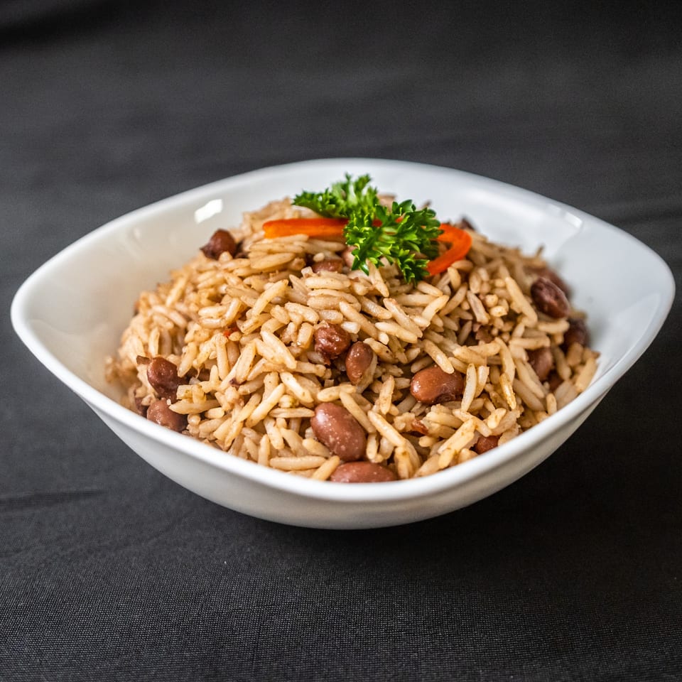 A white bowl filled with rice and beans, garnished with parsley and red pepper strips.