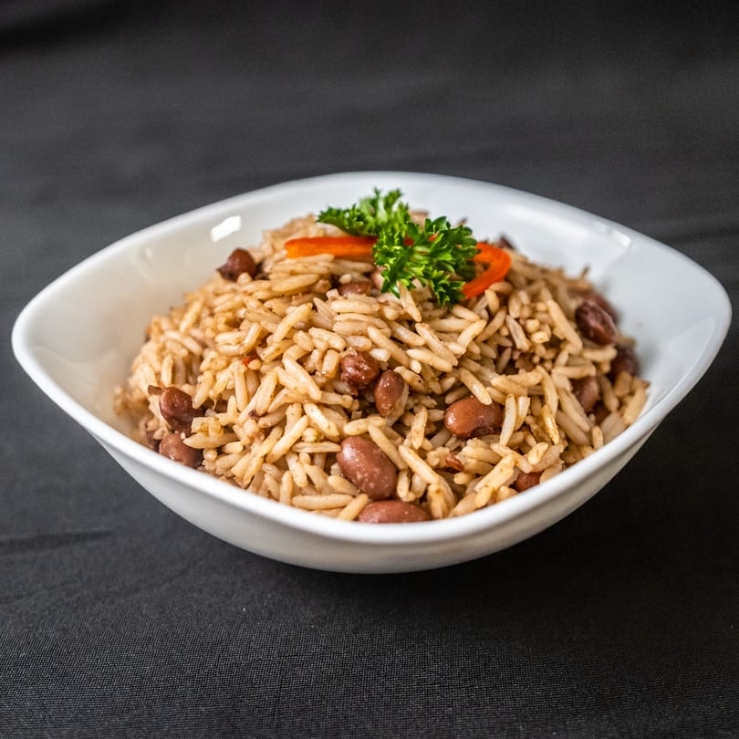 A white bowl filled with rice and beans, garnished with parsley and red pepper strips.