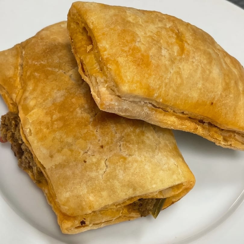 Two golden-brown, flaky pastries filled with a savory meat mixture, served on a white plate.