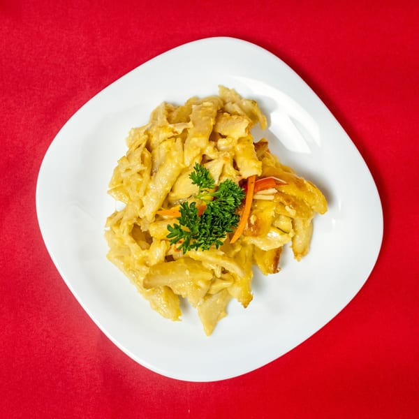 A white plate with yellow pasta, garnished with parsley and carrot strips, on a red background.
