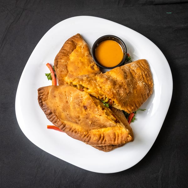 Three golden-brown empanadas, one cut open to show filling, served with a side of orange dipping sauce.