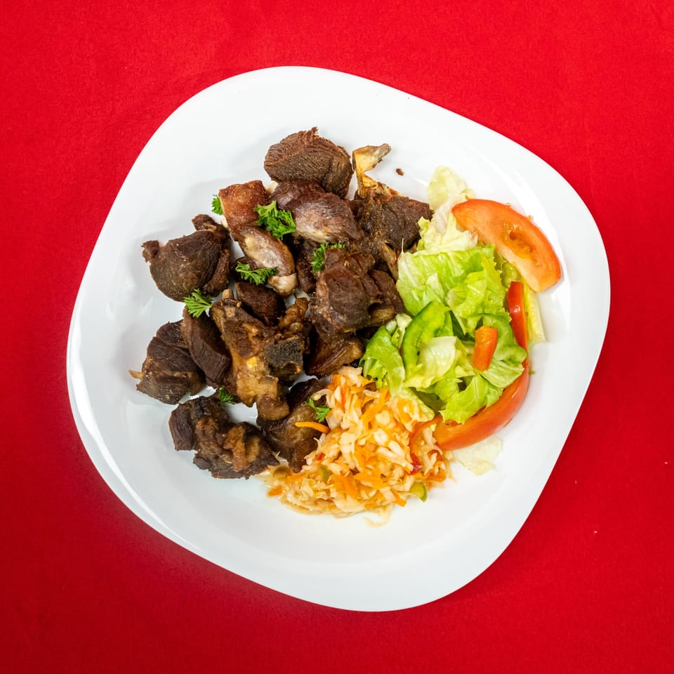 Crispy fried goat meat with a side of fresh green salad and coleslaw on a white plate.