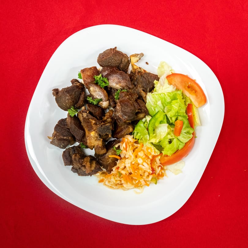 Crispy fried goat meat with a side of fresh green salad and coleslaw on a white plate.