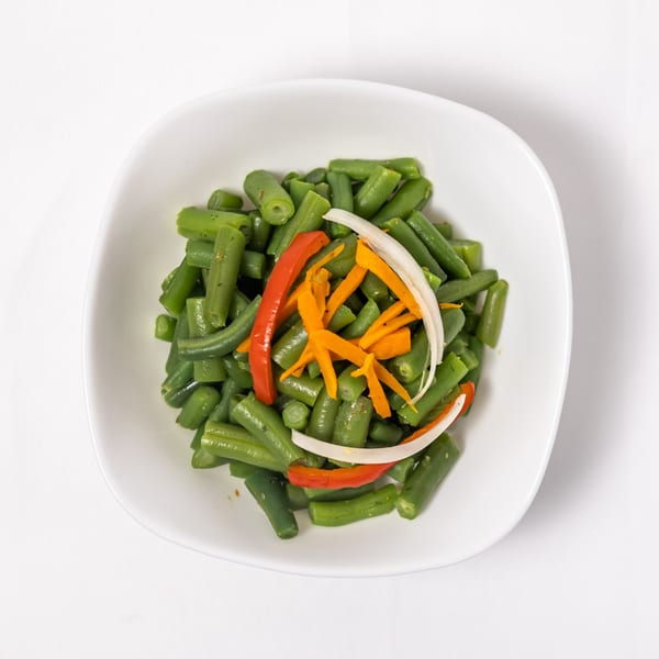 Green beans with julienned carrots, red bell pepper, and white onion in a white bowl.