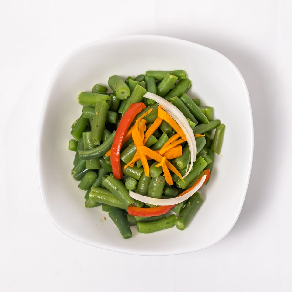 Green beans with julienned carrots, red bell pepper, and white onion in a white bowl.