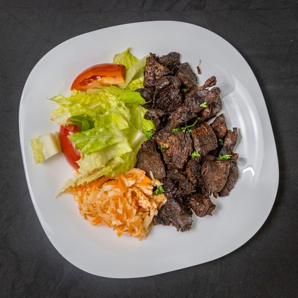Grilled beef chunks with fresh lettuce, tomato, and shredded cabbage salad on a white plate.