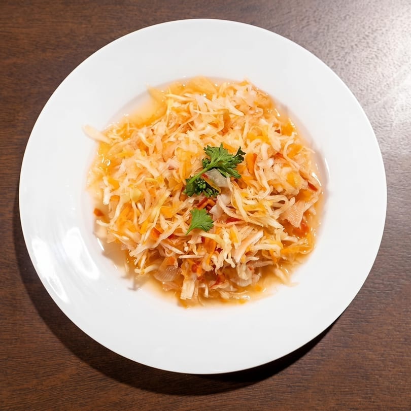 A white plate holds a vibrant salad of shredded cabbage and carrots, garnished with fresh cilantro.