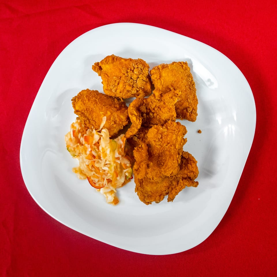 Crispy fried chicken pieces and coleslaw on a white plate against a vibrant red background.