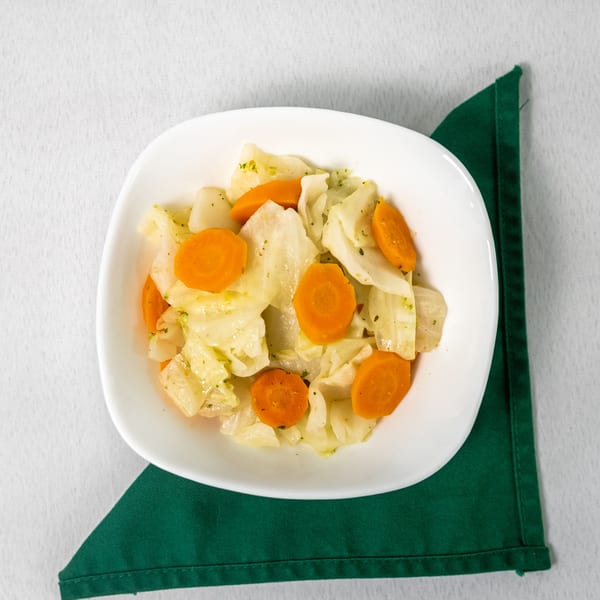 Overhead view of a white bowl filled with cooked cabbage and sliced carrots on a green napkin.