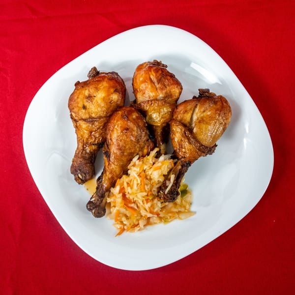 Four crispy fried chicken drumsticks with a side of coleslaw on a white plate.